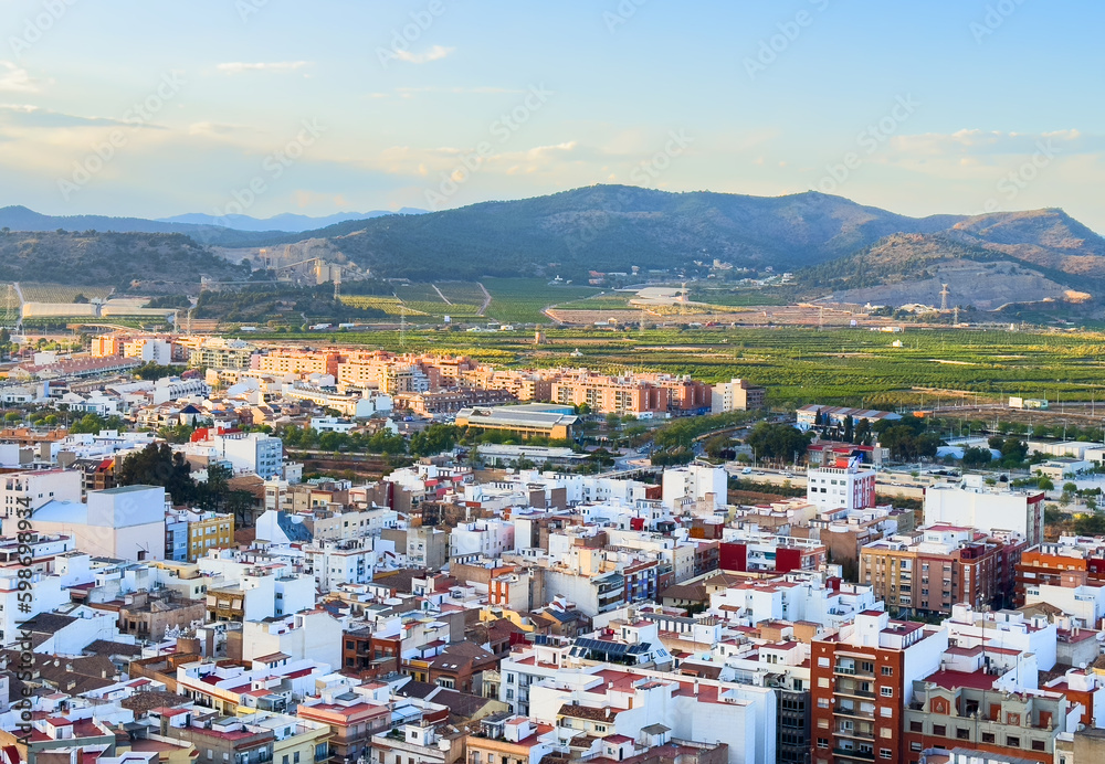 Buildings, houses and streets in city, aerial view. View of rooftops and streets of city of Sagunto in Spain. Town against backdrop of mountains. Roofs of houses and roofs from side of Sagunto Castle.