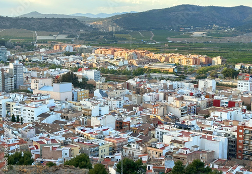 Buildings, houses and streets in city, aerial view. View of rooftops and streets of city of Sagunto in Spain. Town against backdrop of mountains. Roofs of houses and roofs from side of Sagunto Castle. © MaxSafaniuk