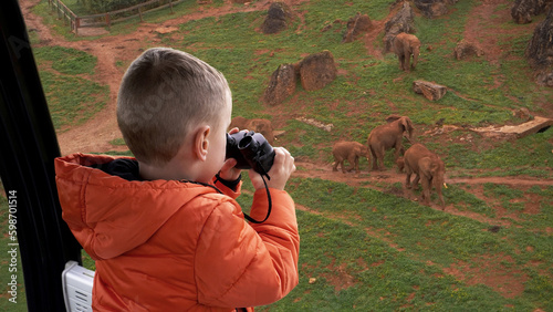  A boy watching wild elephants with binoculars from the funicular