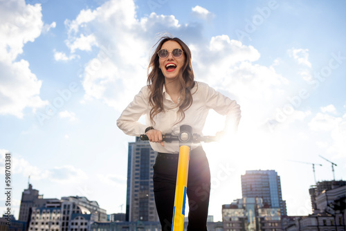 young happy girl in sunglasses rides forward on electric scooter and shouts in the street, woman uses eco transport