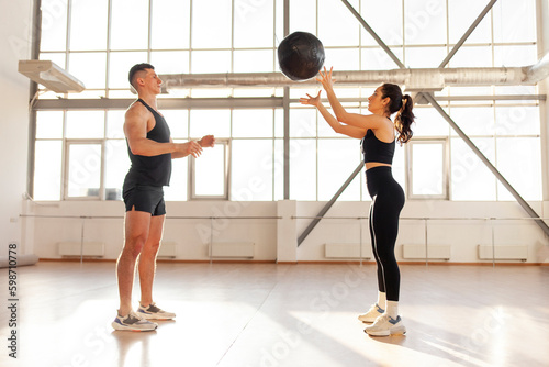 athletic couple in sportswear at crossfit training throw the ball in the room, woman and man together at fitness