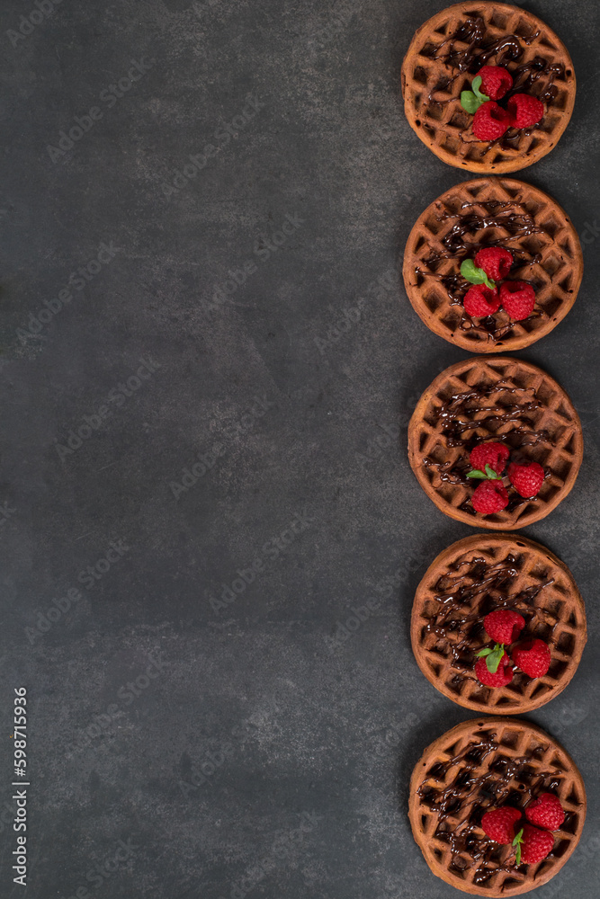 Round Chocolate waffles with raspberries. Dark gray background. Top view. Copy space