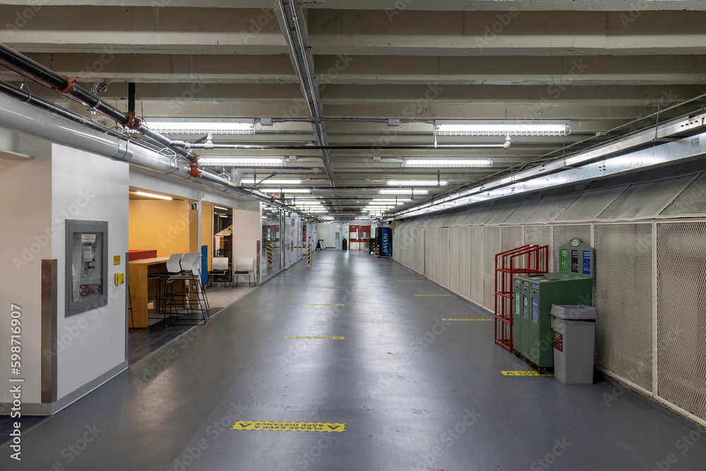 View down a long underground tunnel with grey polished concrete floors, overhead fluorescent lighting, nobody