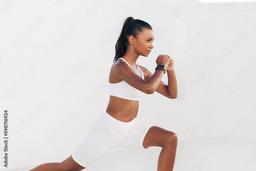 Young woman practicing flexibility exercises outdoors. Side view of a slim female warming up in a white outdoor studio.