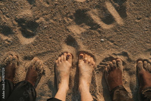 Three pairs of bare feet black and white skin different race nationality friends on sea shore sand photo