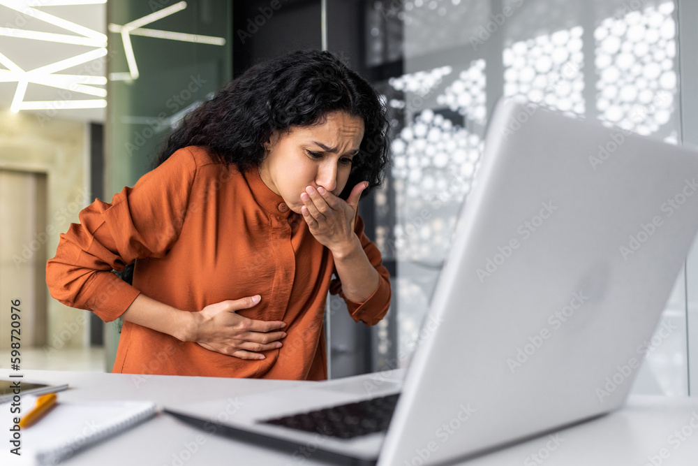 Sick business woman working at work, having severe nausea and abdominal pain, latin american working inside office building using laptop Sick business woman working at work, having severe nausea and abdominal pain, latin american working inside office building using laptop