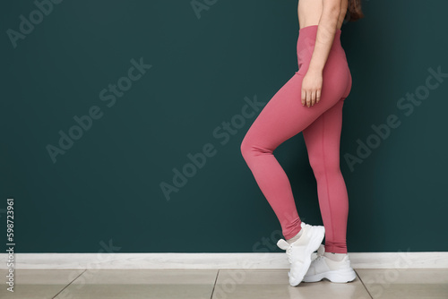 Sporty young woman in leggings near green wall