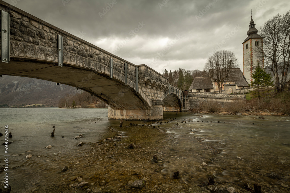 Dark cloudy sunny evening with no colors near Bohinj lake with old bridge