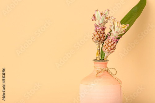 Vase with decorative pineapples and palm leaf on beige background