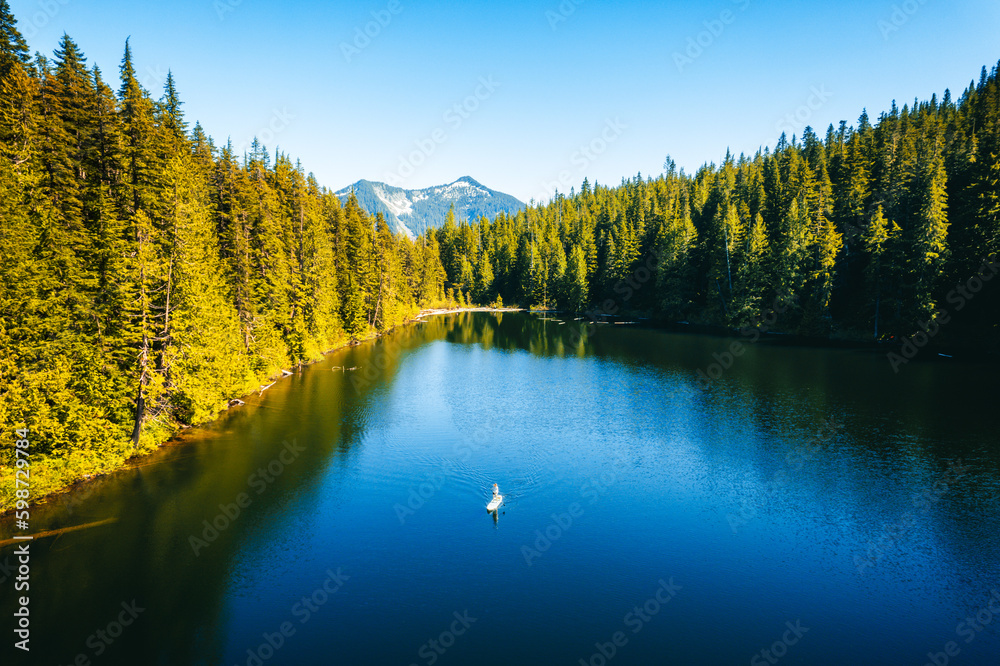 A woman paddleborading on Talapus Lake of the Alpine Lake Wilderness  with Cedars and Hemlock trees on the mountain side in Washington State.