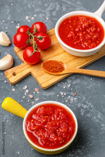 Bowls with tasty tomato sauce and fresh vegetables on blue background
