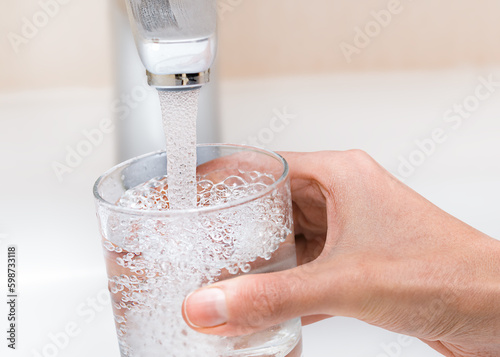female hand pour water from the tap into a glass