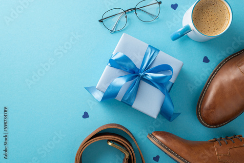Fashionable Father's Day idea. Top view of gift package, leather shoes, accessories, belt, spectacles, coffee mug on blue background with space for text