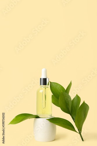 Bottle of cosmetic oil with plant twig and stand on yellow background