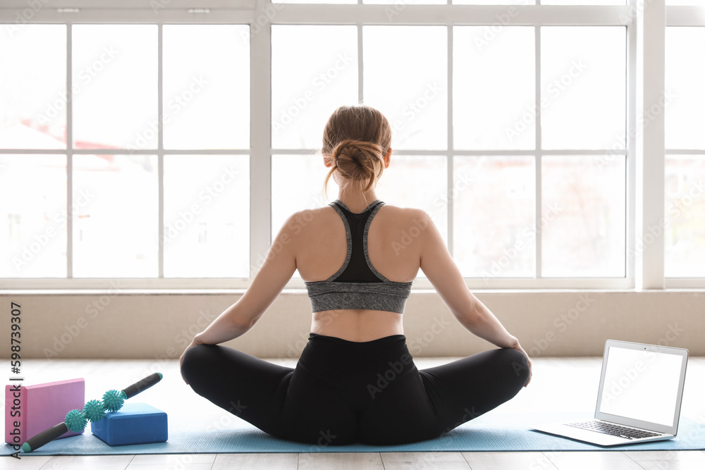 Sporty young woman with laptop doing yoga in gym, back view Sporty young woman with laptop doing yoga in gym, back view