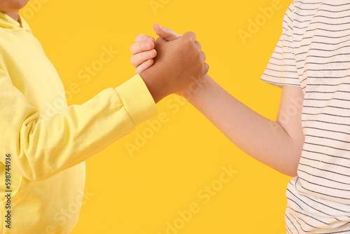 Fototapeta Naklejka Na Ścianę i Meble -  Little boys holding hands on yellow background, closeup. Children's Day celebration