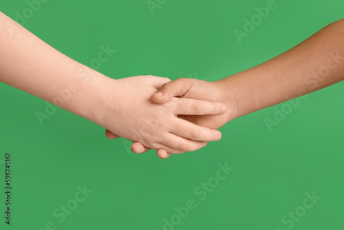 Little boys shaking hands on green background, closeup. Children's Day celebration