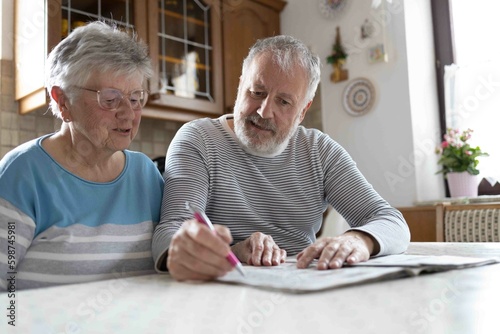 Grey haired senior couple making sudoku in the kitchen 