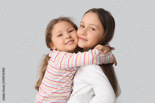 Cute little sisters hugging on light background, closeup