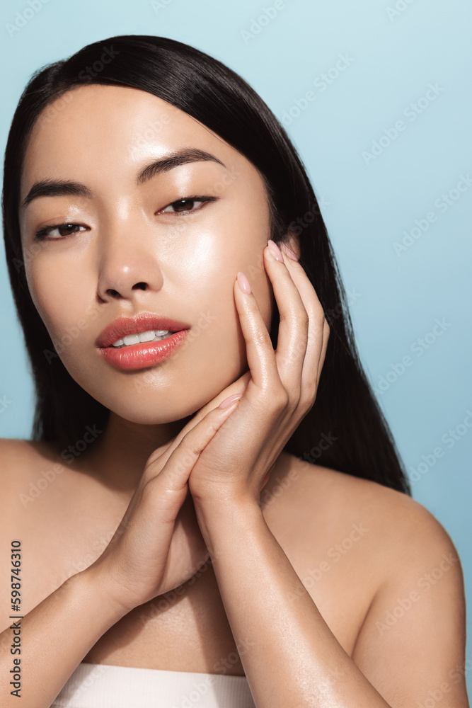 Vertical shot of young asian woman, model touches her clean glowing skin, washing face, takes-off makeup with skincare cosmetic products and smiles with confidence at camera, blue background Vertical shot of young asian woman, model touches her clean glowing skin, washing face, takes-off makeup with skincare cosmetic products and smiles with confidence at camera, blue background