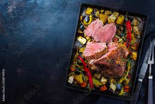 Traditional Greek barbecue leg of lamb with vegetable and feta cheese served as top view on a rustic tray with copy space left