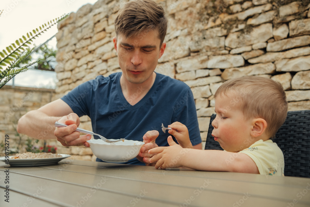 
dad and child have breakfast at the table in the yard with oatmeal
