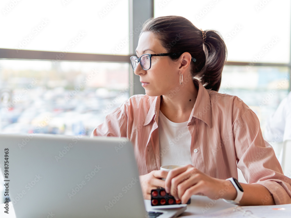Mindful woman with medicine pills. Working with laptop. Mental health problems, emotional burnout or headache. Modern office at co-working center. Workplace for freelancers or students. Mindful woman with medicine pills. Working with laptop. Mental health problems, emotional burnout or headache. Modern office at co-working center. Workplace for freelancers or students.