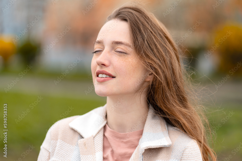 Cute beautiful woman with closed eyes enjoying sunny day outdoors. Young female on street