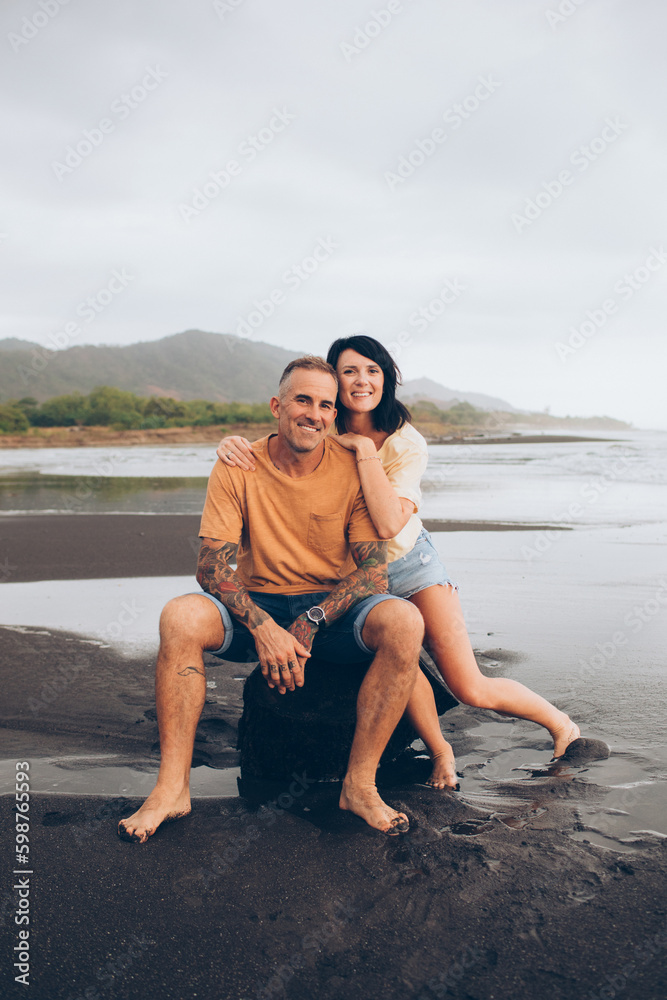 couple sitting on a rock smiling at the camera at the beach