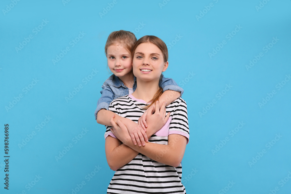 Little daughter hugging her mom on light blue background. Happy Mother's Day Little daughter hugging her mom on light blue background. Happy Mother's Day