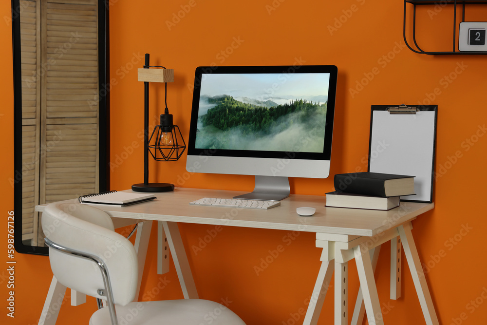 Workplace with modern computer on wooden desk and comfortable chair near orange wall. Home office Workplace with modern computer on wooden desk and comfortable chair near orange wall. Home office