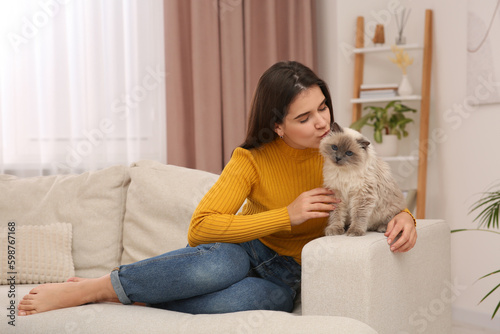 Woman kissing her cute cat on comfortable sofa at home