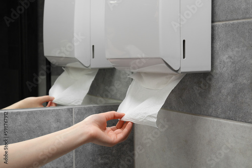 Woman taking new fresh paper towel from dispenser in bathroom, closeup photo