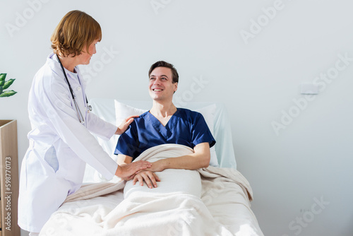 the doctor is examining the patient in the hospital. Caucasian female doctor talking to male patient lying in hospital bed.