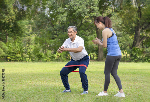 young woman trainer teaching a senior man doing exercise with elastic band,smiling woman applauding beside him,legs stretch exercise for rehabilitation muscles in older adult,concept of elderly health © Verin