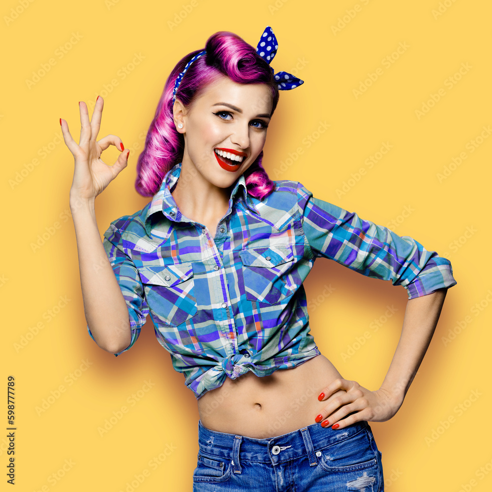 Pin up girl. Portrait photo of excited cheerful smiling red purple hair woman show ok okay hand sign gesture. Retro and vintage concept. Yellow background. Female model at studio.