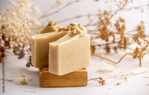 Delicate natural beige handmade soap in a wooden soap dish on a white background with flowers and petals.