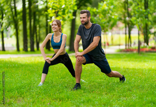 Image of young smiling couple, woman training with man or bearded coach trainer, doing squat fit exercise together, look forward direction, outdoor. Fitness, sport, workout, healthy lifestyle concept.