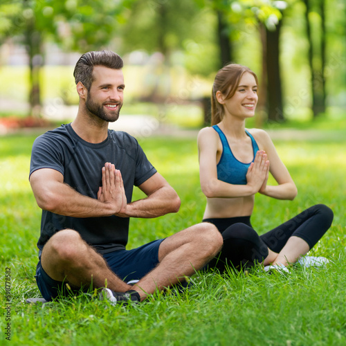 Full body image - young smiling couple sitting in lotus position or woman practicing with man, male bearded coach trainer, doing yoga exercises or meditating together, after outside training. Square.