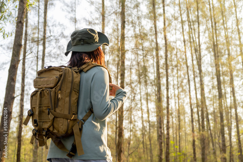 Young Asian girl with a backpack and hat hiking in the mountains during the summer season, a traveler walking in the forest. Travel, adventure, and journey concept. © maya1313