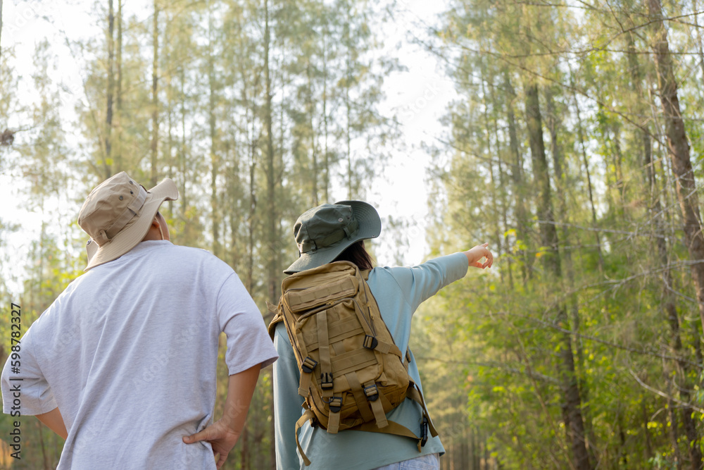 Young Asian man and woman with a backpack and hat hiking in the mountains during the summer season, a traveler walking in the forest. Travel, adventure, and journey concept.