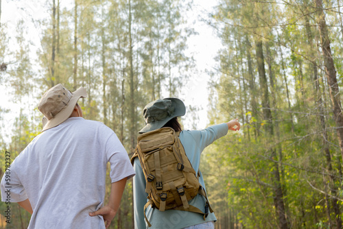 Young Asian man and woman with a backpack and hat hiking in the mountains during the summer season, a traveler walking in the forest. Travel, adventure, and journey concept.