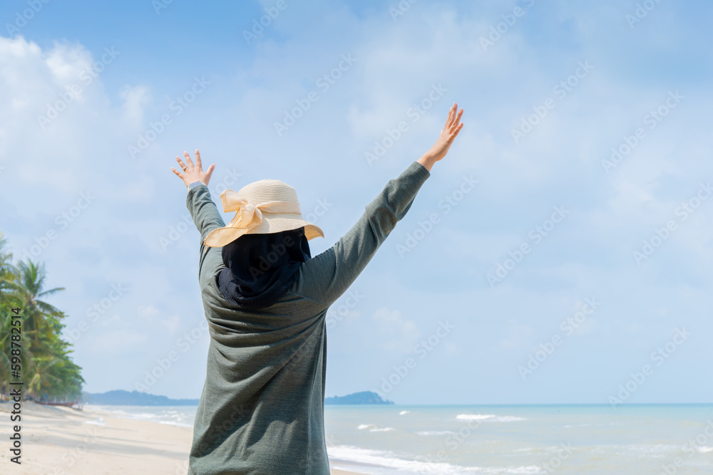 Happy Young muslim woman in grey dress and hat standing on the beach and open hands on sea with breaths a full breast and enjoys freedom. Happy Young muslim woman in grey dress and hat standing on the beach and open hands on sea with breaths a full breast and enjoys freedom.