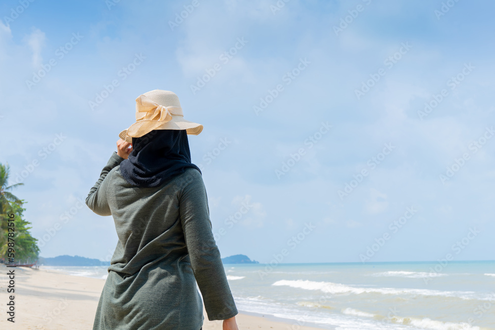 Happy Young muslim woman in a grey dress and hat standing on the beach and enjoying freedom, and looking at the sea.