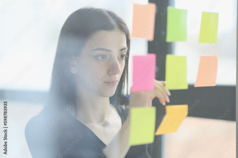 Concentrated woman puts colorful sticky notes on glass wall Concentrated woman puts colorful sticky notes on glass wall
