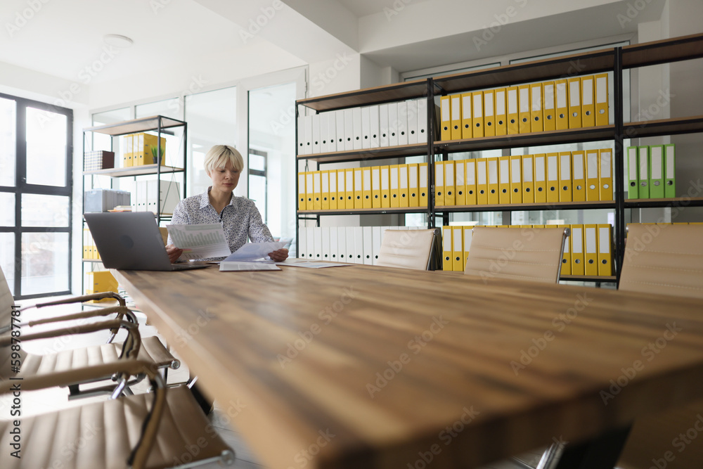 Blonde manager sits at long wooden table studying papers