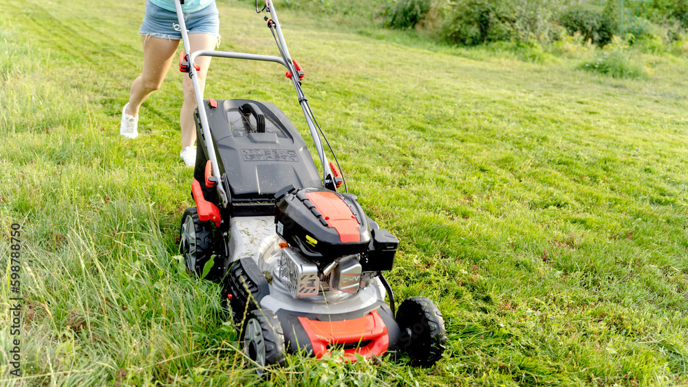 Fototapeta premium a girl with a lawn mower mows a beautiful lawn