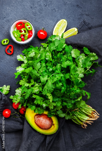 Fresh cilantro or coriander  chili and jalapeno peppers  avocado  lime and cherry tomatoes - ingredients for Mexican spicy cuisine. Black kitchen table background  top view