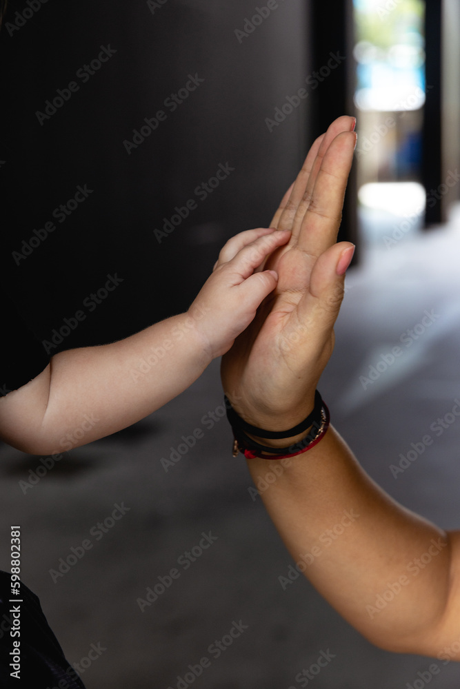 Mother holding hands with her child indoors, closeup. Happy family