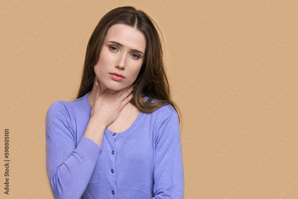 Young woman touching painful neck, sore throat for flu, cold and viral infection, beige background Young woman touching painful neck, sore throat for flu, cold and viral infection, beige background